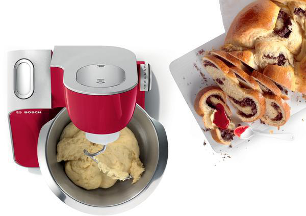 Rote und silberne Küchenmaschine mit Teig in einer Schüssel und geschnittenem Brot.