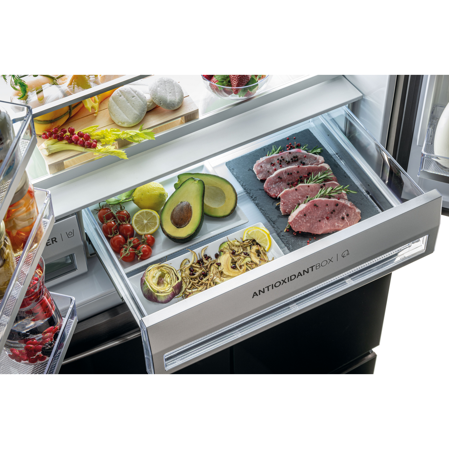 Cajón de refrigerador lleno de comida: carne, aguacate, tomates, queso y otros artículos.