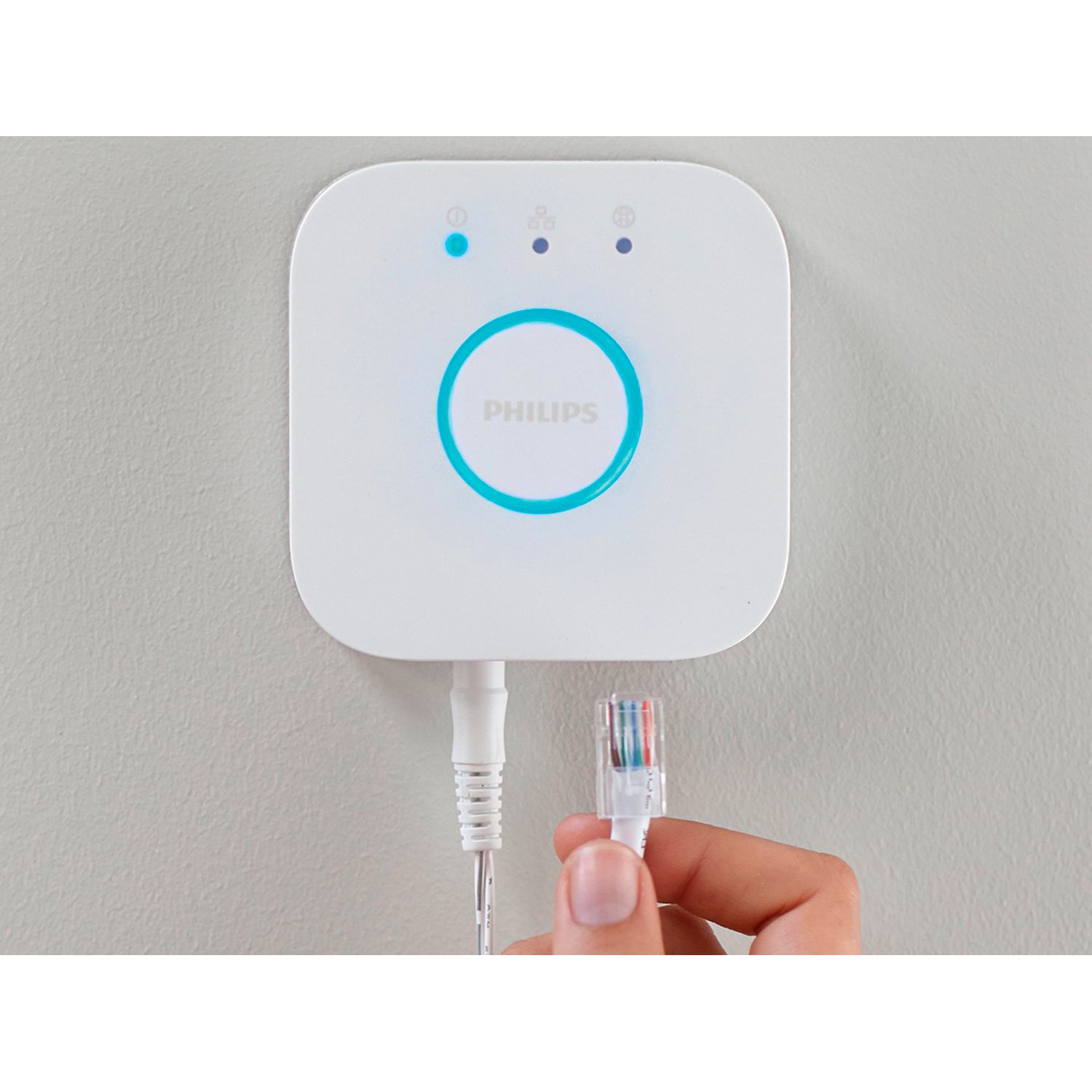 Philips Hue Bridge blanca. Una mano sostiene un cable de red enchufado.