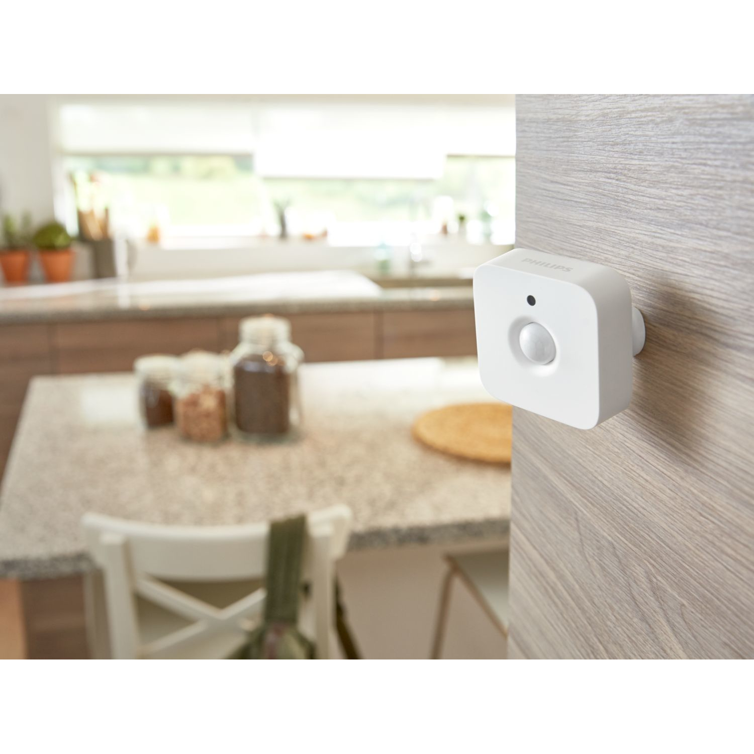 Un sensor de movimiento blanco adherido a una pared de madera, con un fondo de cocina.