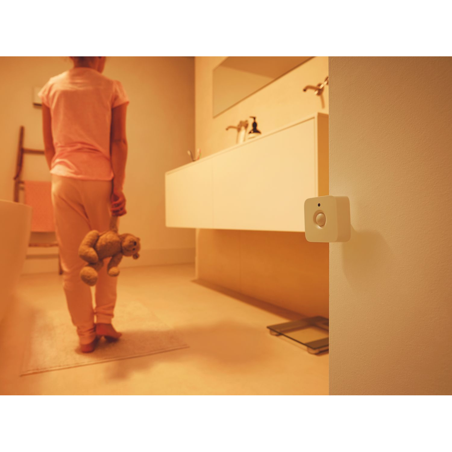 Una persona en un baño, una luz inteligente en la pared y un oso de peluche en el suelo.