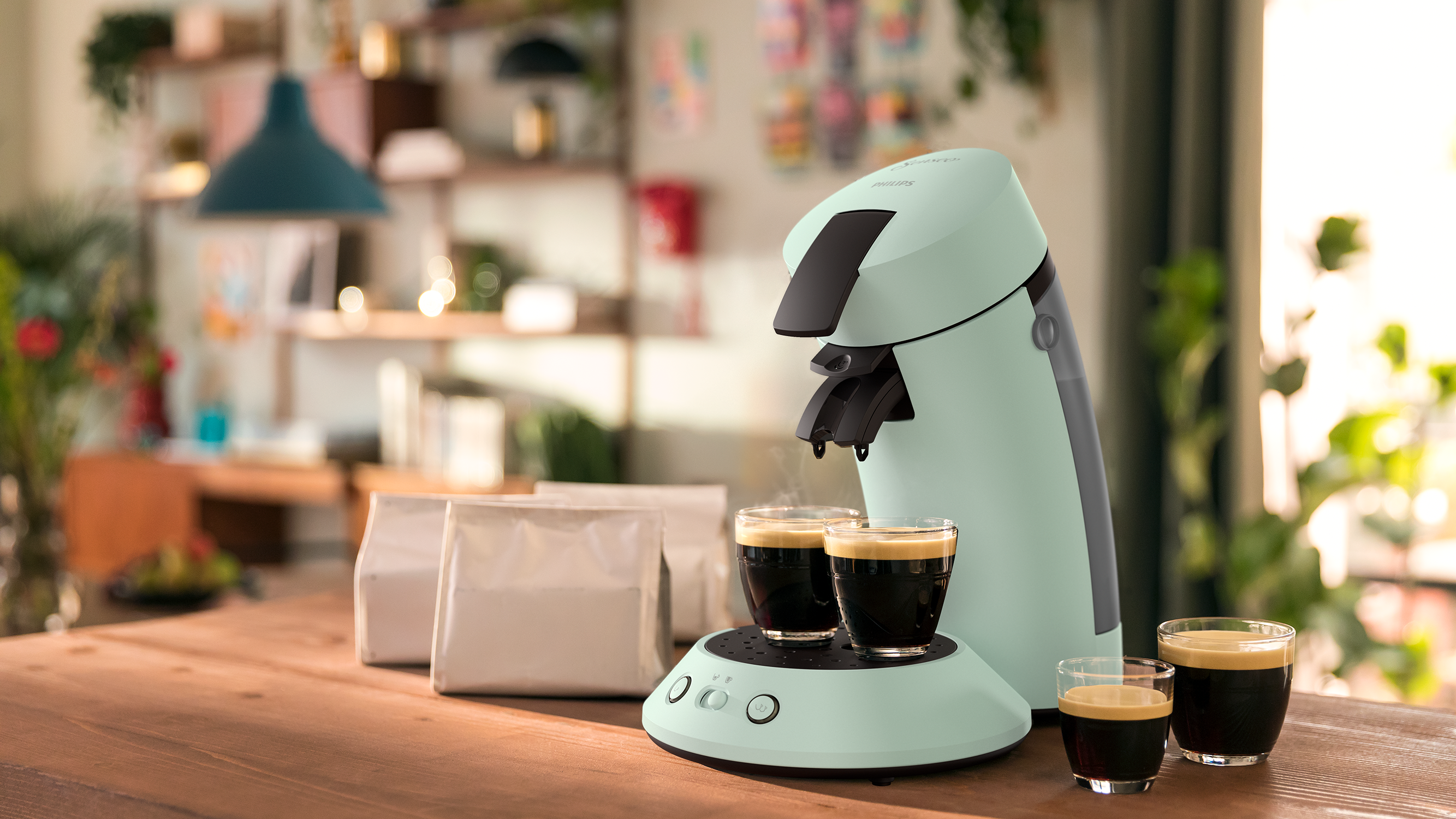 Coffee maker with two cups, and a few coffee bean bags on wooden table.