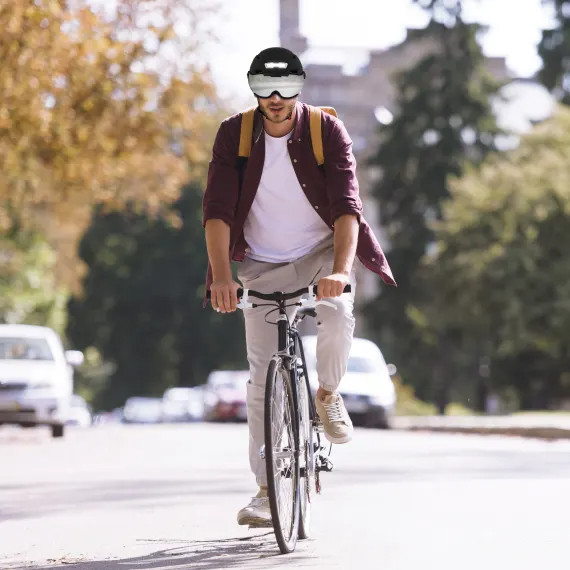 Homme faisant du vélo dans la rue, portant un casque avec des lunettes, face à la caméra.