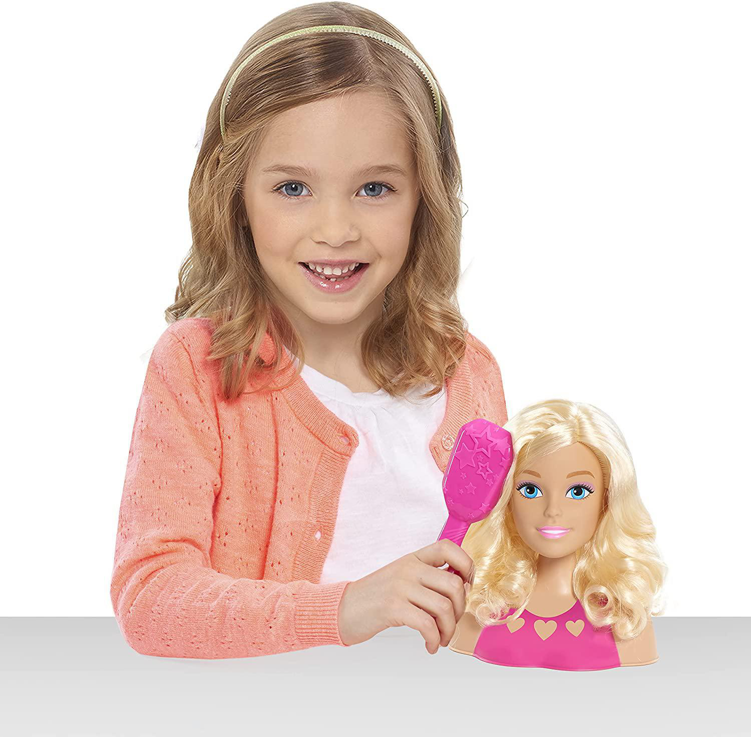 Junges Mädchen mit einem Barbie-Stylingkopf und einer Bürste, weißer Hintergrund.