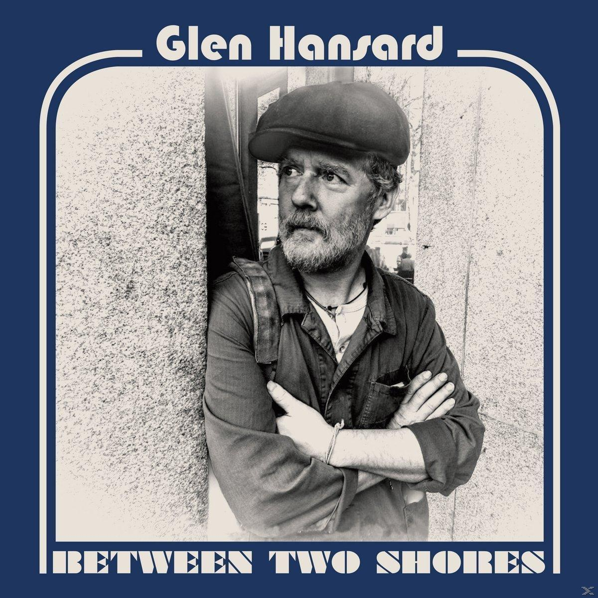 Album cover with Glen Hansard in a cap, arms crossed. Text reads 'Glen Hansard' and 'Between Two Shores' on a blue frame.