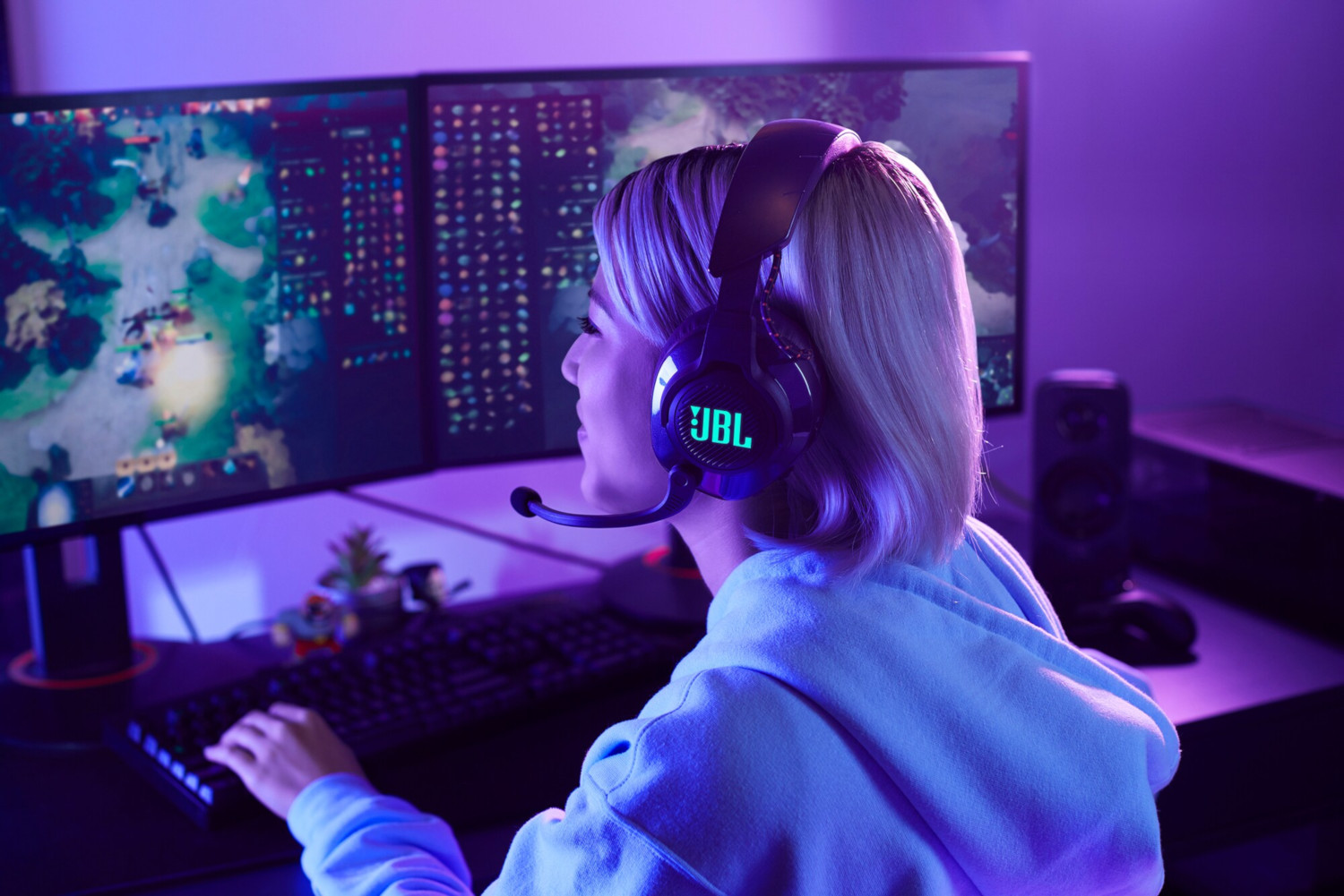 Woman wearing a gaming headset and looking at two computer screens.