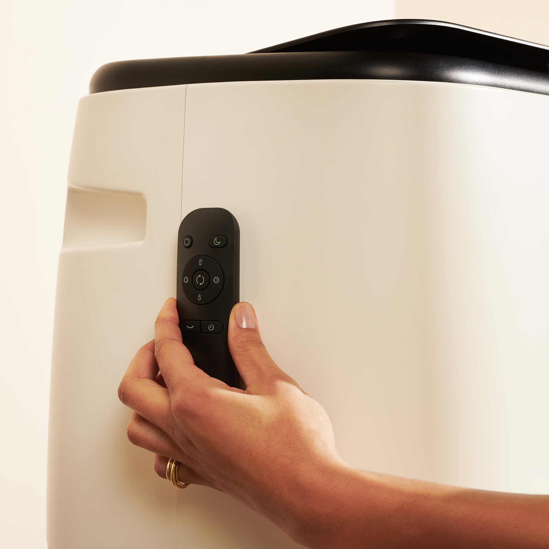 Une main tient une télécommande noire à côté d'un purificateur d'air blanc. La télécommande comporte plusieurs boutons et icônes.