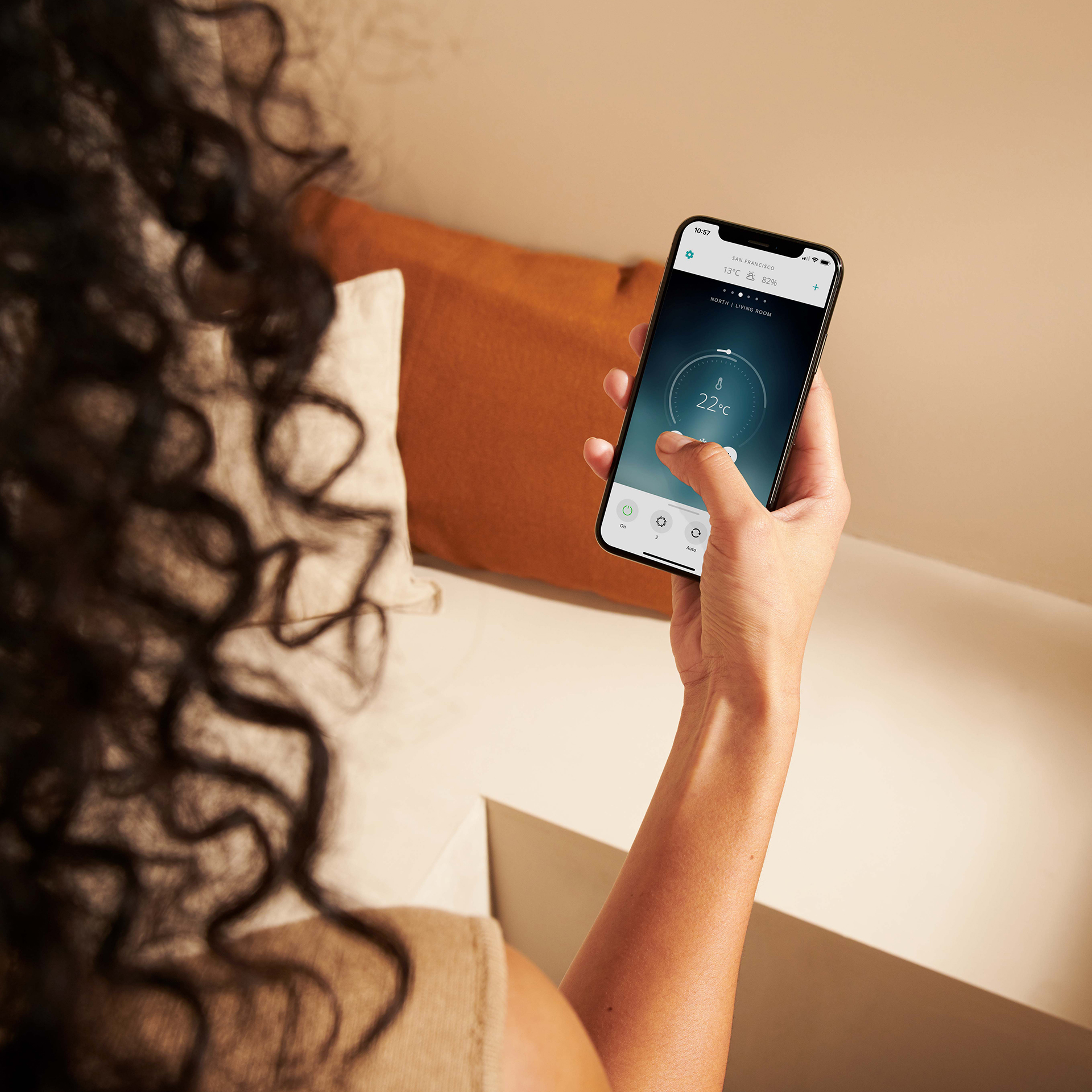 Une main tenant un téléphone affichant un thermostat intelligent. La température ambiante est de 22°C. Des cheveux sont visibles.