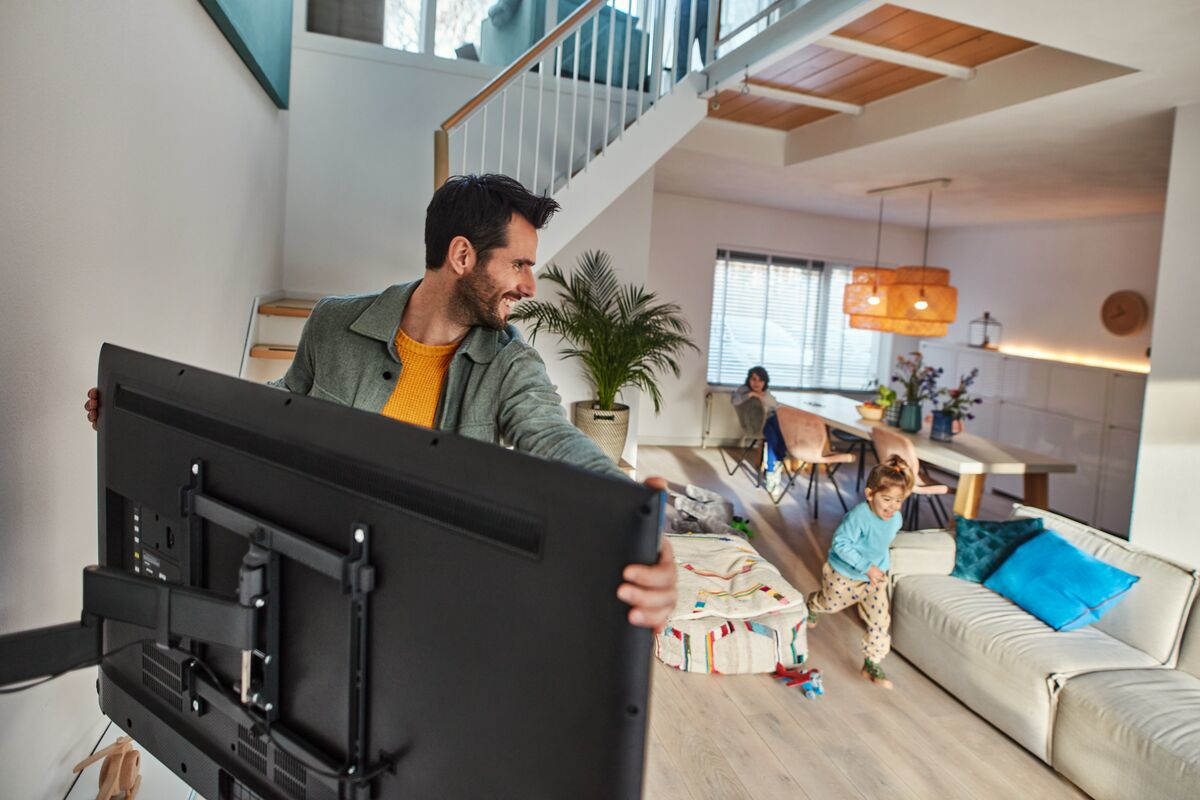 Een man monteert een grote tv aan de muur van een woonkamer.