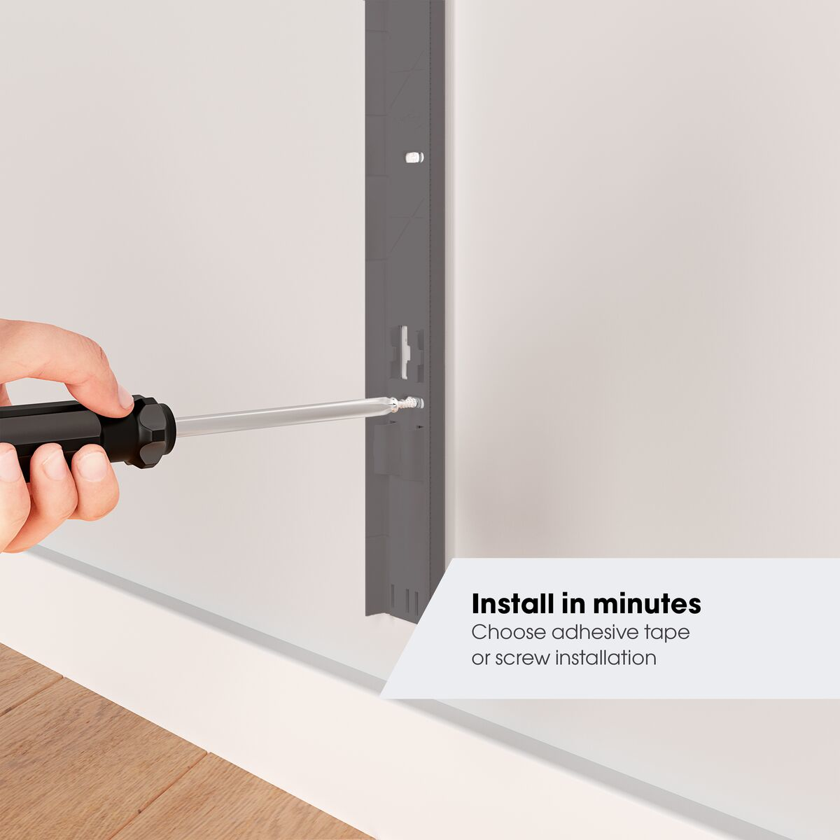 Une main utilise un tournevis pour installer un support mural gris sur un mur blanc.