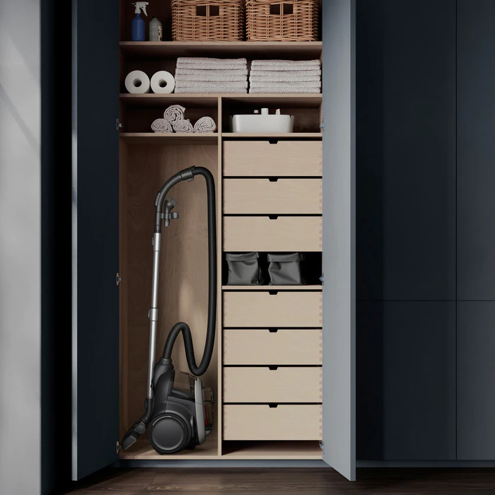 An open wardrobe with shelves, drawers, a vacuum cleaner, and folded towels. The color scheme is dark blue and light wood.