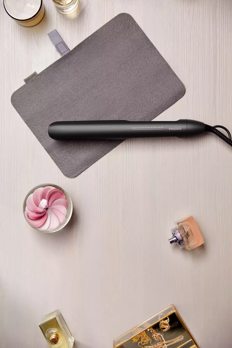 Fer à lisser, étui gris, parfum et cosmétiques sur une table en bois.