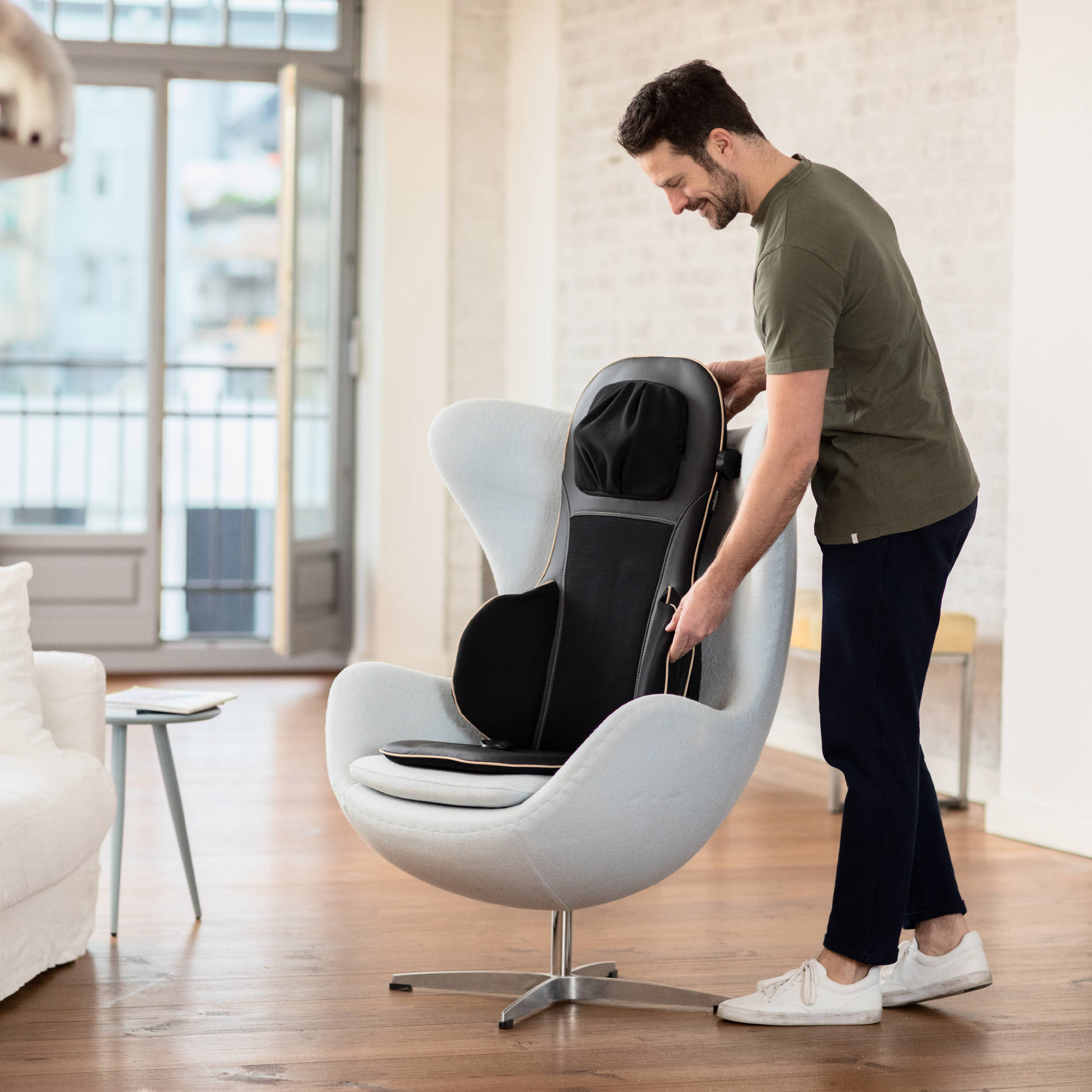 Ein Rückenmassagegerät auf einem weißen Eiersessel in einem gut beleuchteten Wohnzimmer.
