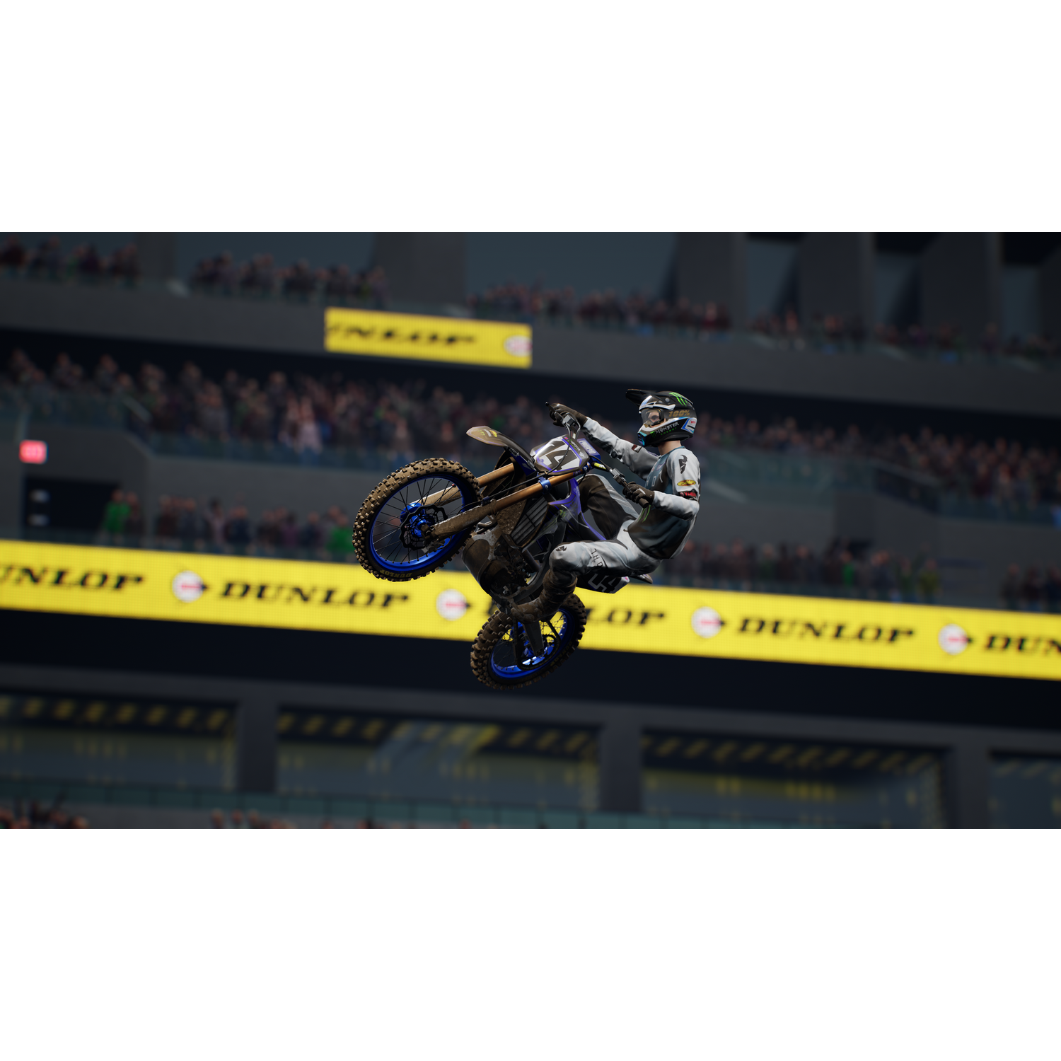 Piloto de motocross en el aire, realizando una acrobacia, sobre un estadio con público.