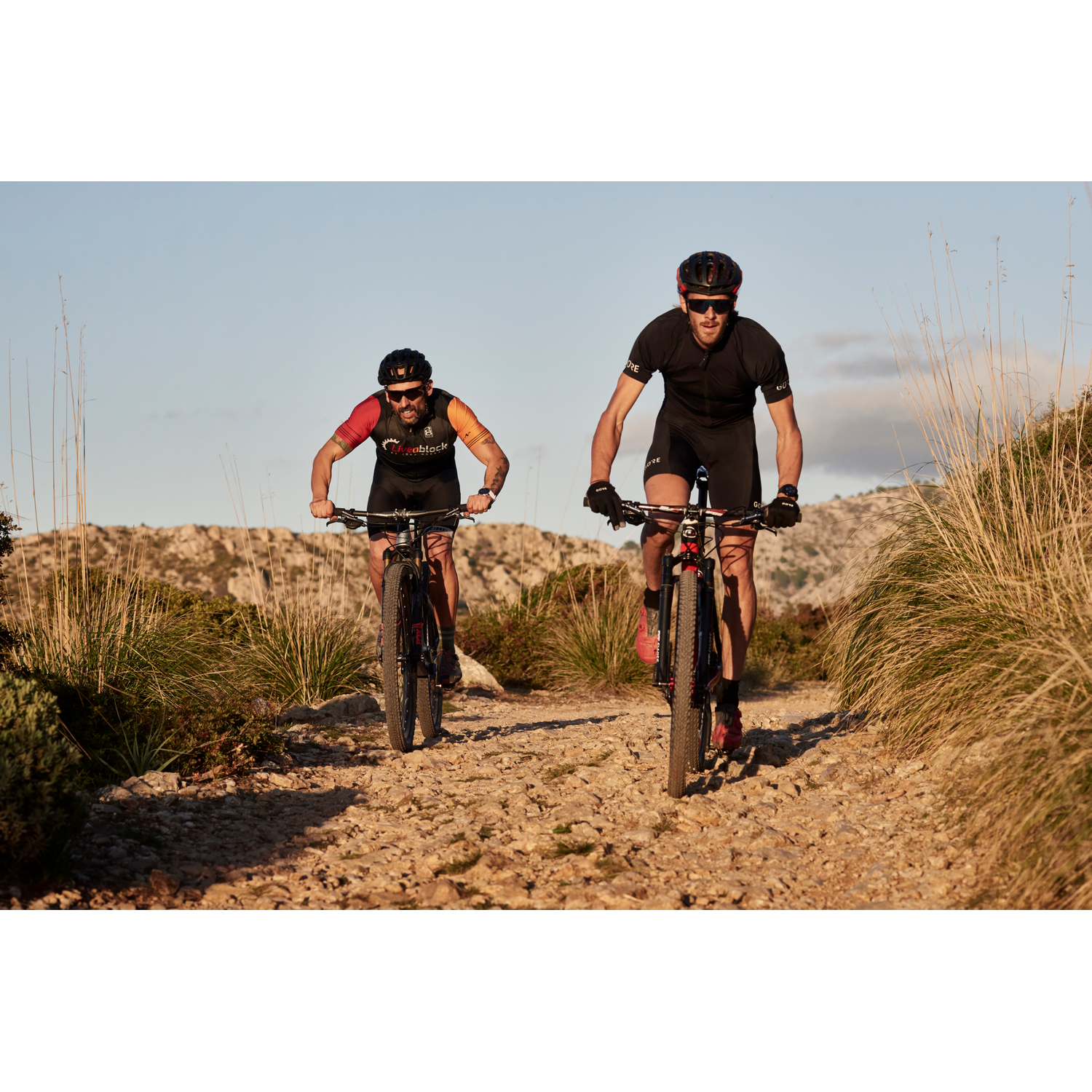 Dos ciclistas montando bicicletas de montaña en un camino de tierra, día soleado.