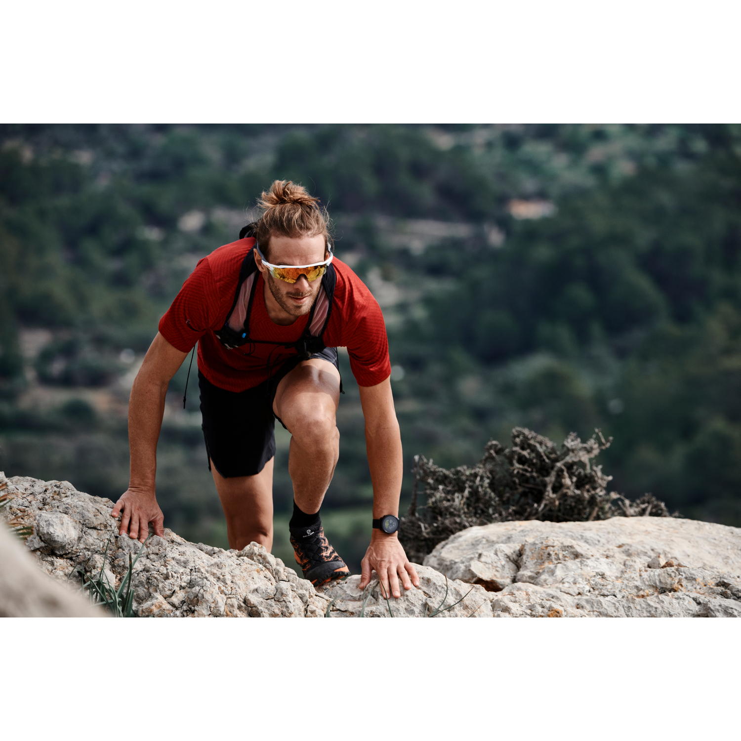Un hombre camina cuesta arriba sobre rocas, con camisa roja y gafas de sol, con reloj.