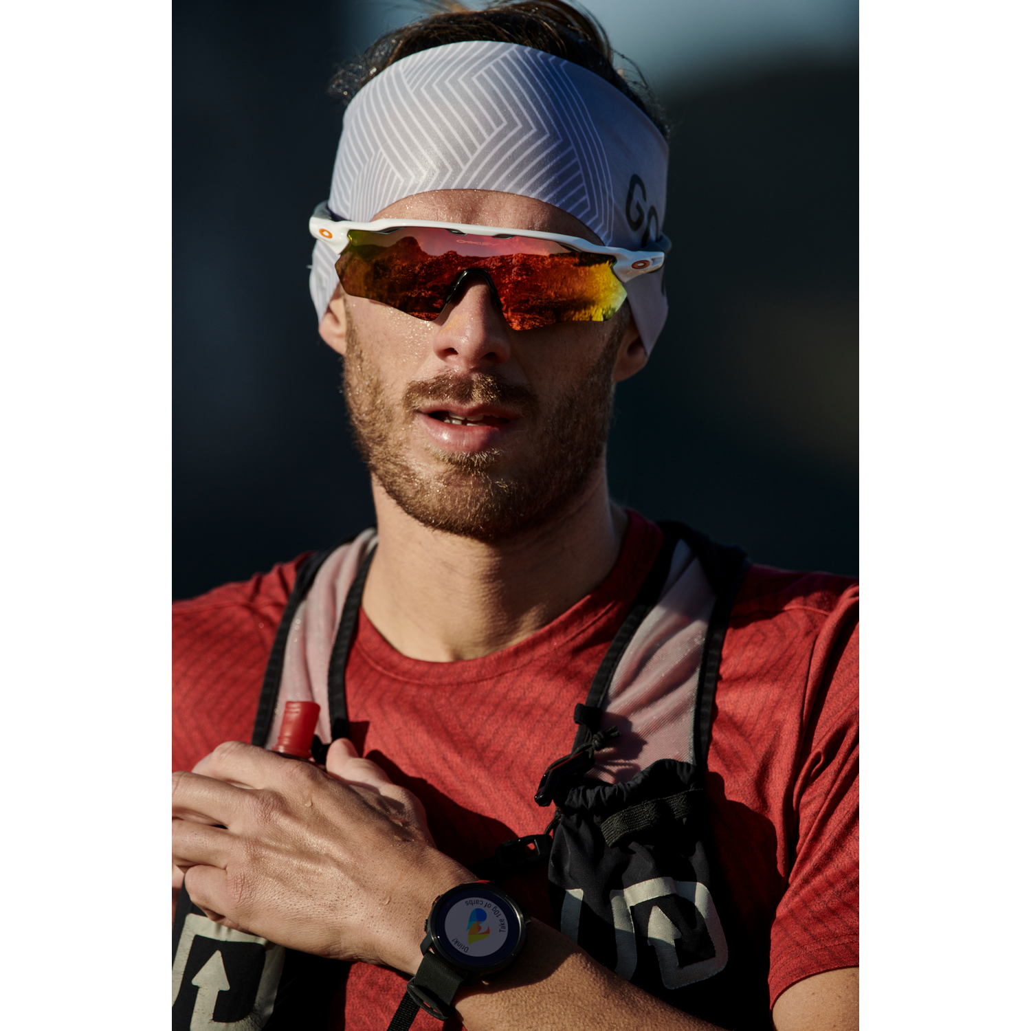 Corredor con gafas de sol y diadema. Mira hacia adelante, con una camisa roja.