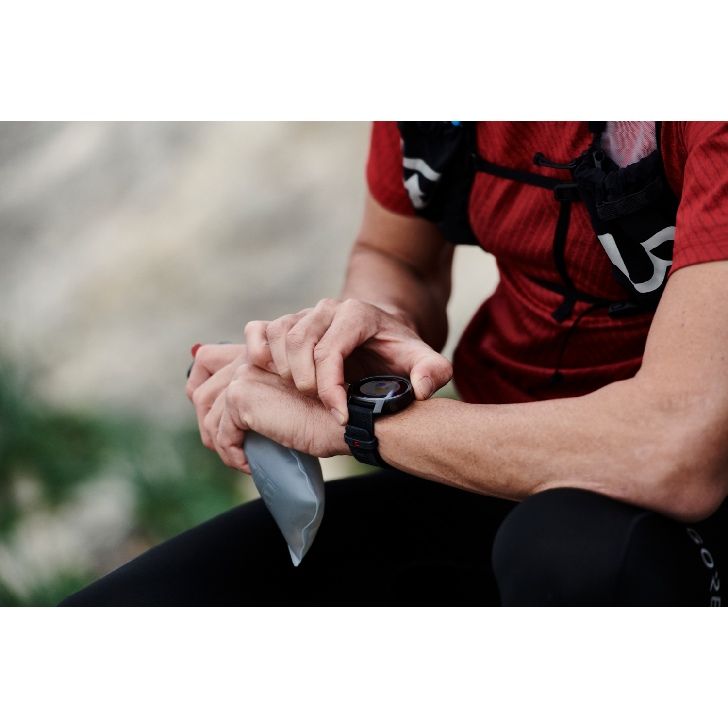 Persona con camisa roja y reloj negro, revisando su smartwatch negro.