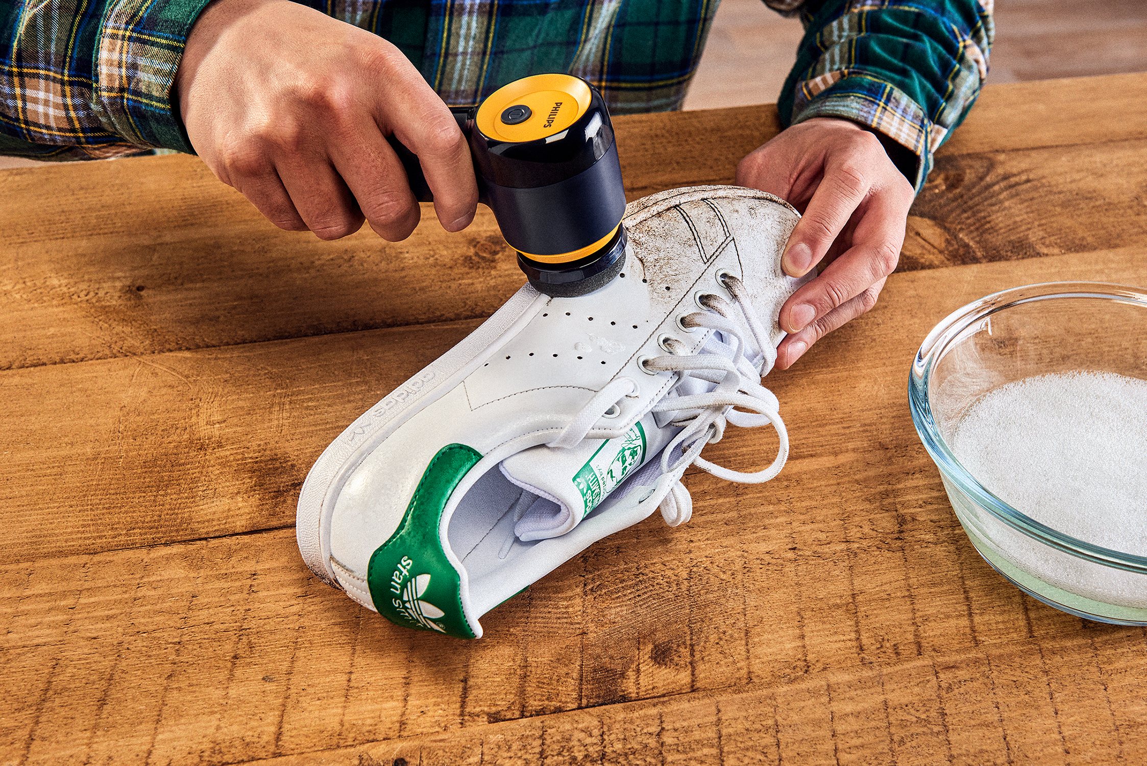 Een persoon die een witte schoen schoonmaakt met een zwart-gele schoonmaaktool.