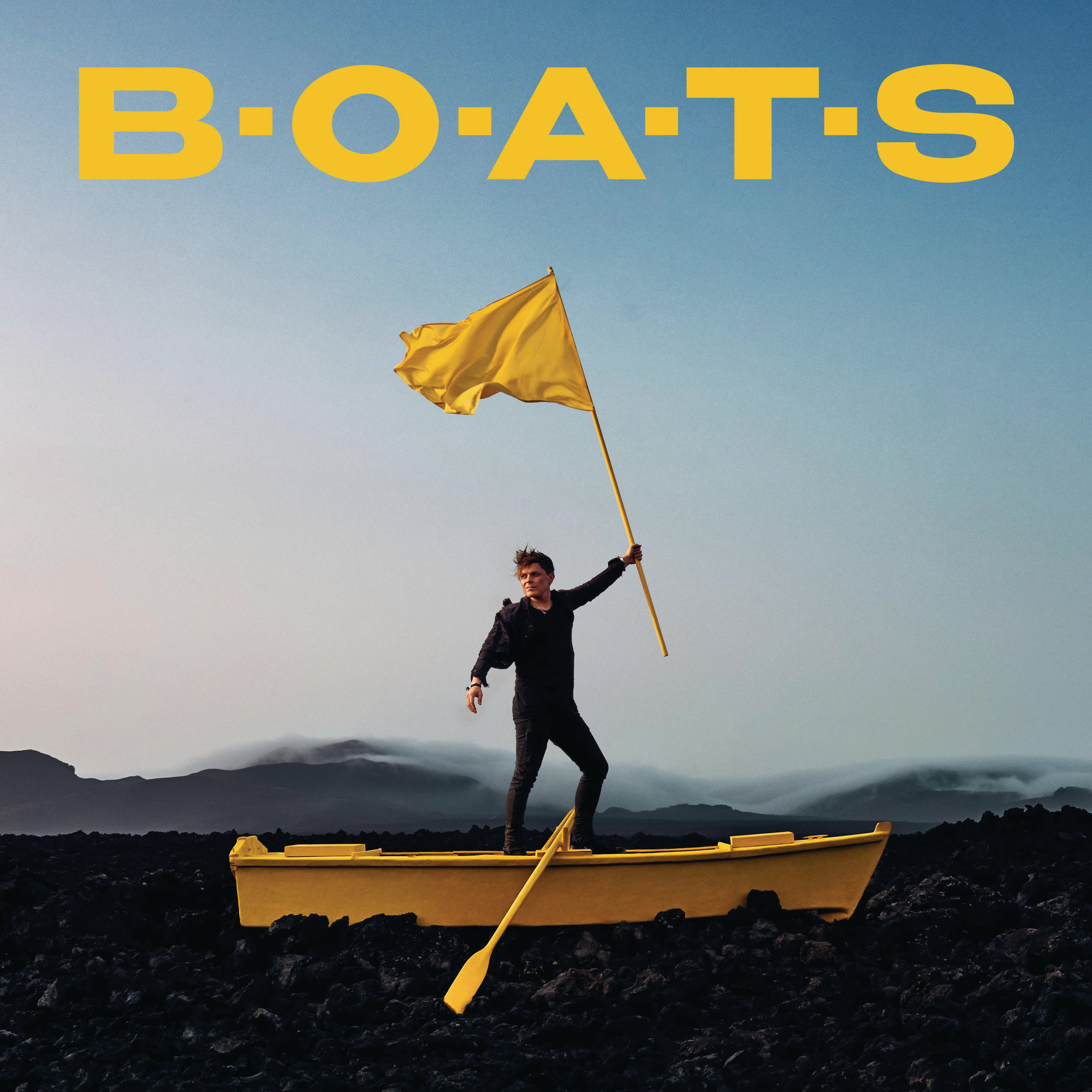 Ein Mann in einem gelben Boot hält eine gelbe Flagge, mit 'BOATS' in gelben Buchstaben darüber, auf blauem Himmel.