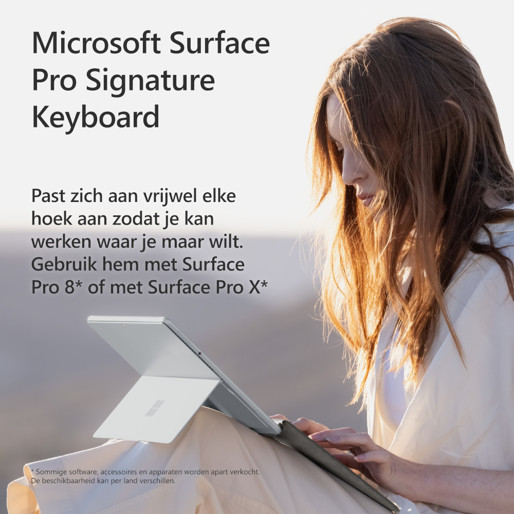 Woman using a silver laptop. Sunlight in the background. Product placement, Microsoft Surface keyboard.