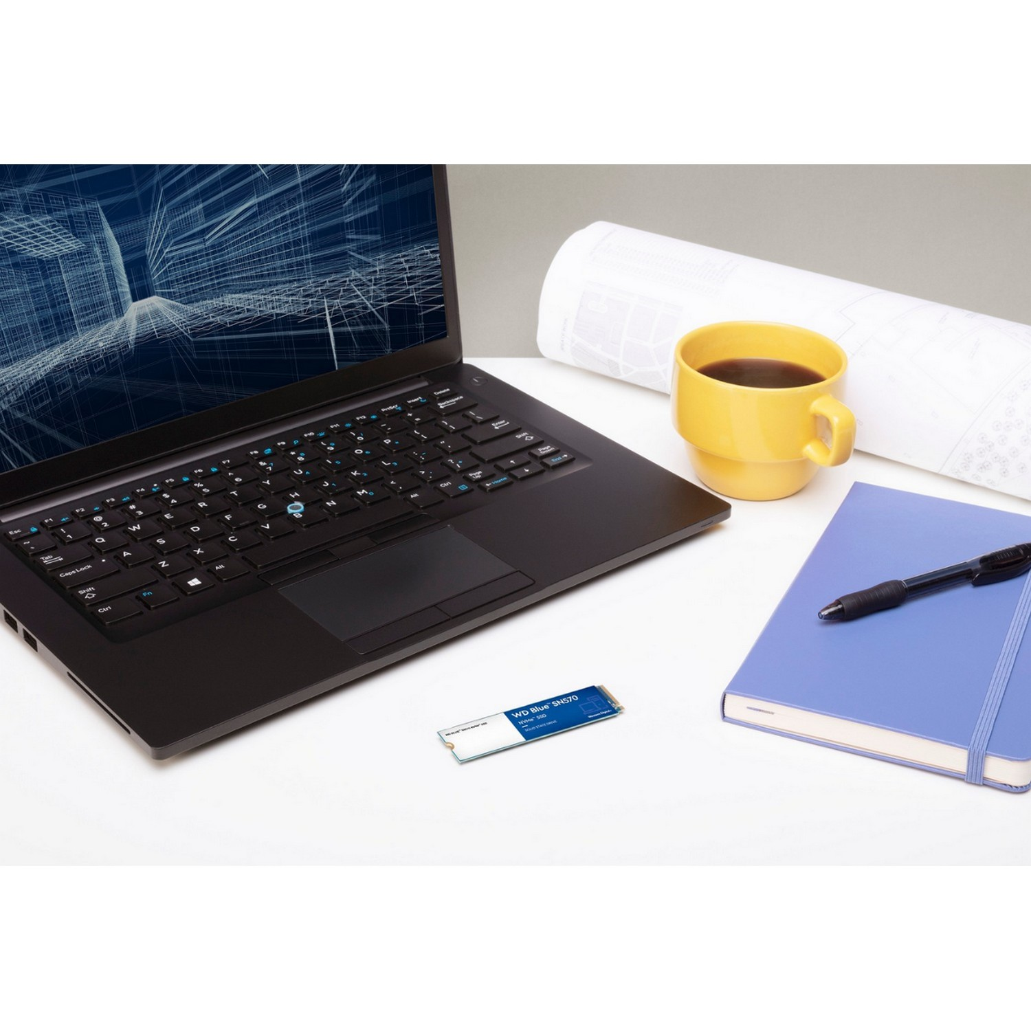 Un portátil, una taza de café, un cuaderno azul y un disco duro externo en un escritorio blanco.