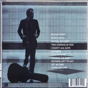 Die Rückseite einer CD-Hülle mit einem Mann in Schwarz in der Nähe einer U-Bahn. Titelliste sichtbar, mit Gitarrenkoffer.