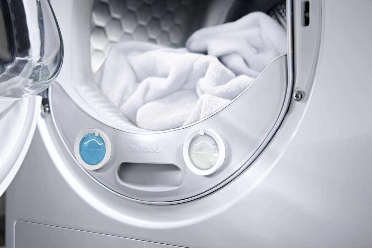 Weiße Wäsche in einer offenen Miele-Waschmaschine mit blauen und weißen Drehknöpfen.