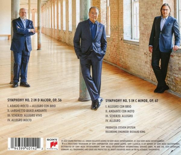 Drei Männer in Anzügen, die in einem Industrieraum stehen. Text über Musik auf der linken Seite.