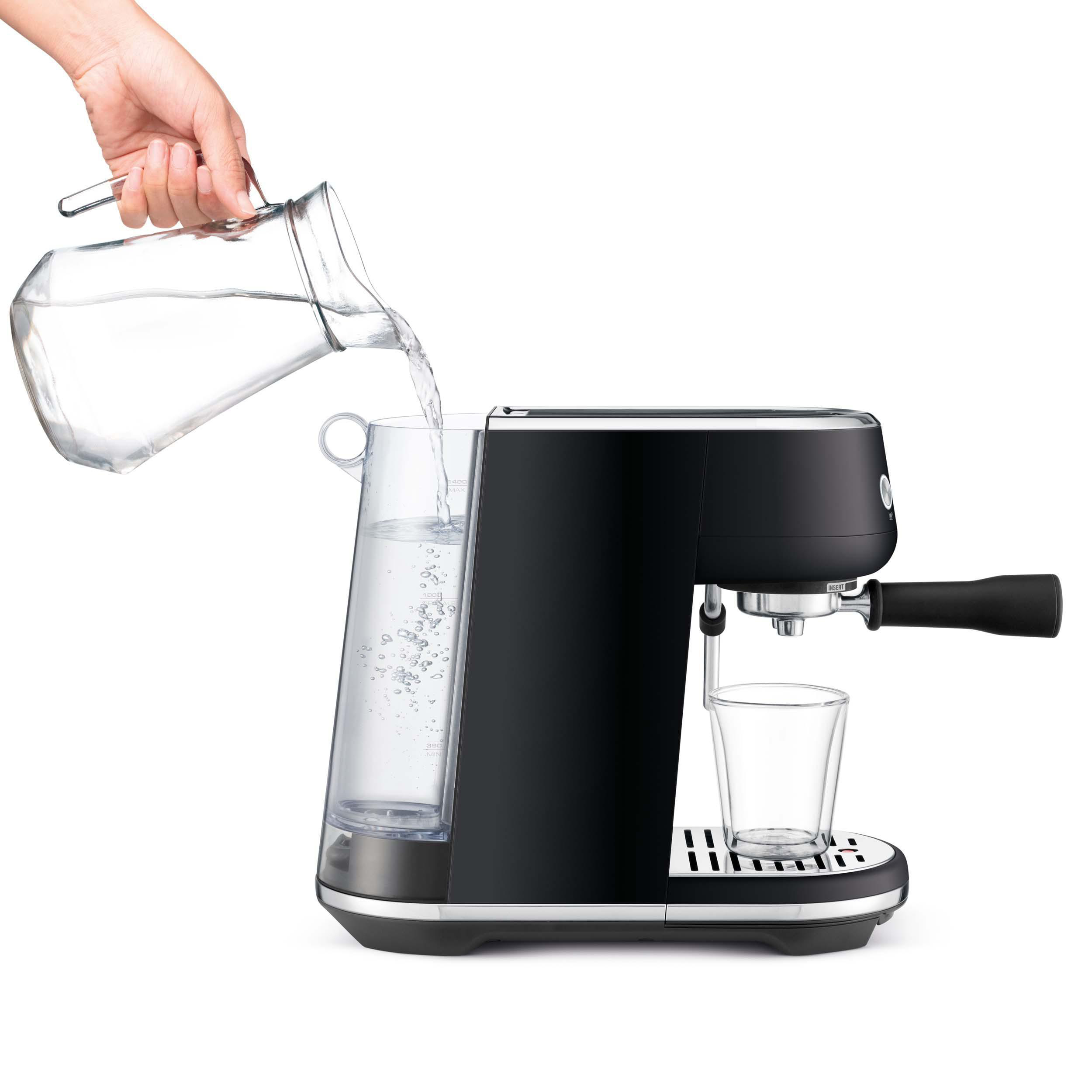 Eine Person gießt Wasser in eine schwarze Espressomaschine mit Glasbehälter.