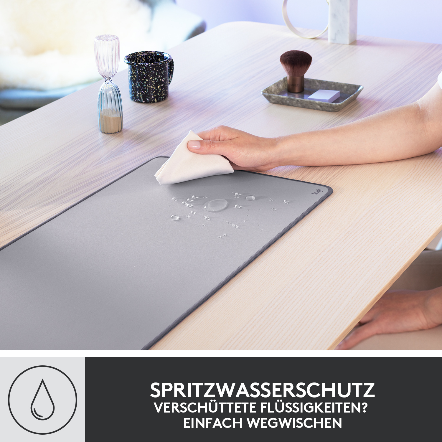 Eine Person wischt eine graue Matte mit einem weißen Tuch ab, Wassertropfen auf der Matte, Holztisch.