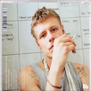Mann mit Zigarette, Tätowierungen am Arm. Im Hintergrund eine Tafel.