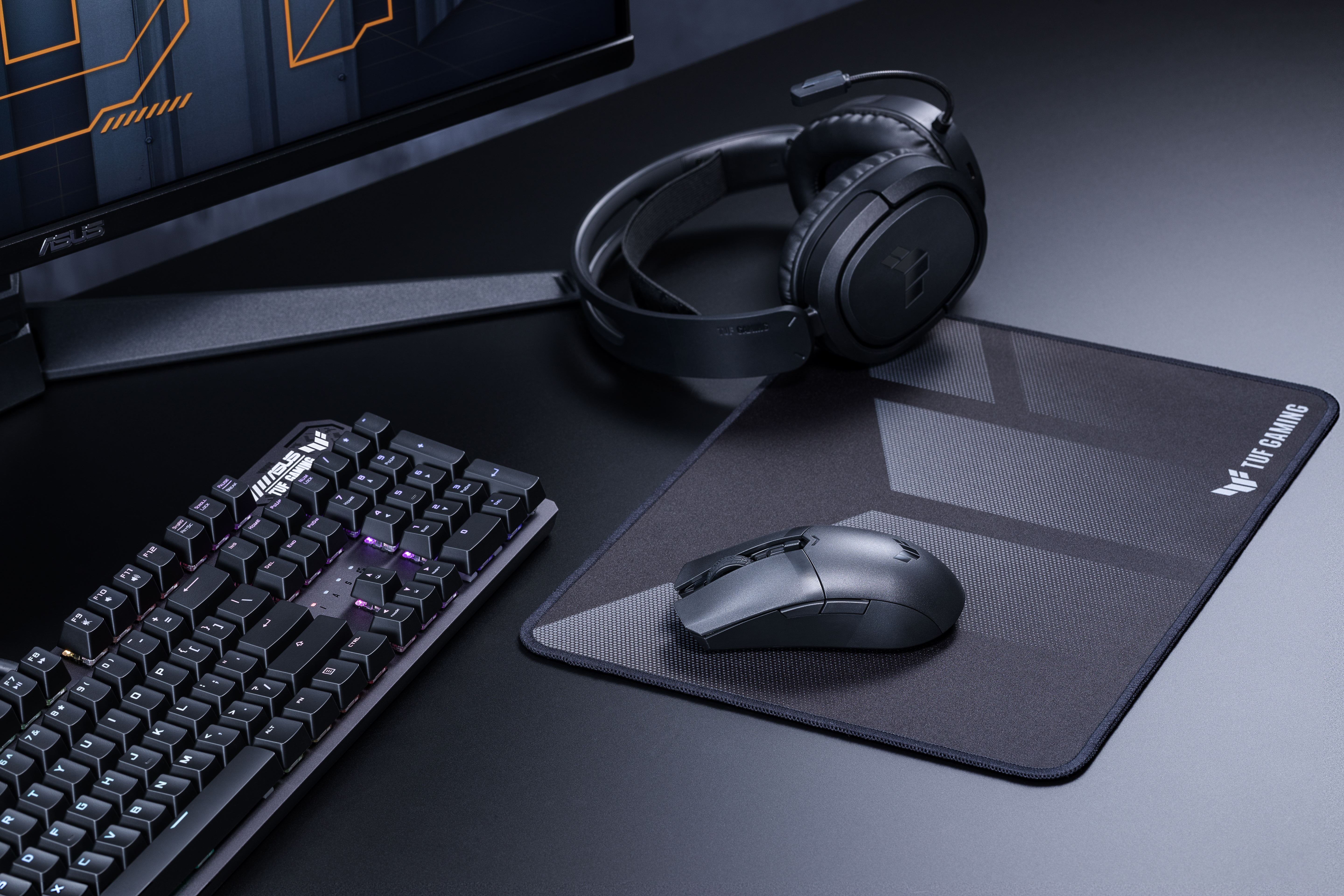 Schwarze Gaming-Tastatur, Maus, Kopfhörer und Mauspad auf einem dunklen Schreibtisch.