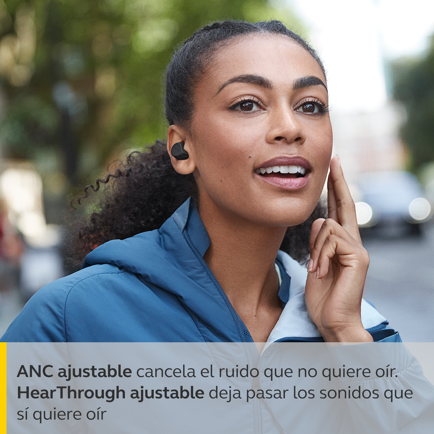Mujer con auriculares negros, tocando la oreja, sonriendo afuera. Texto sobre cancelación de ruido.