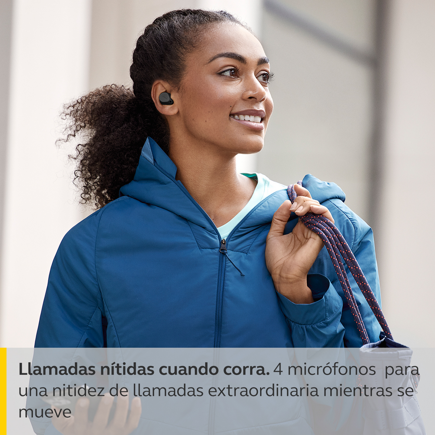 Mujer con auriculares sonríe. Lleva una chaqueta azul y lleva un bolso.