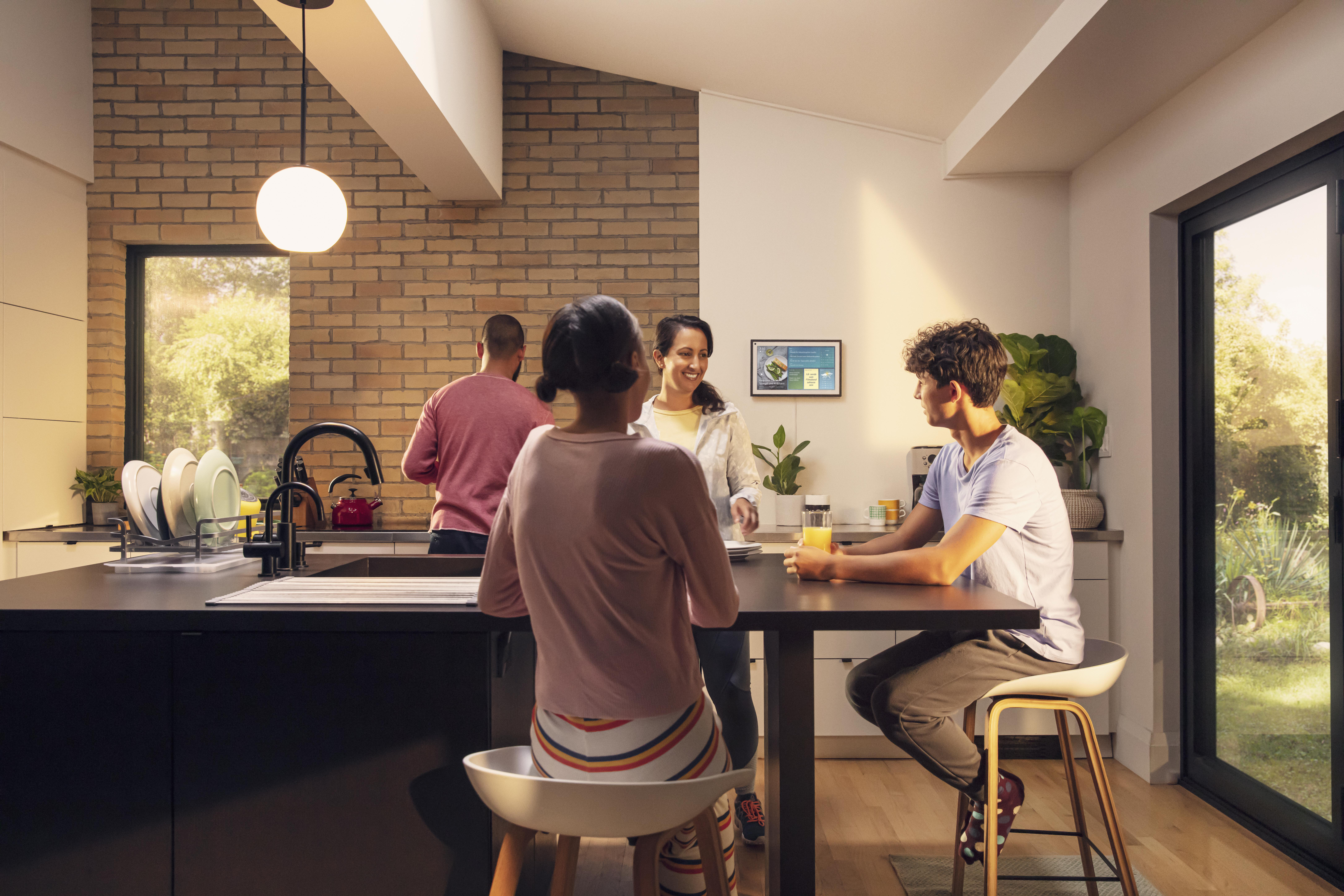 Familie in der Küche, Ziegelmauer, Kücheninsel, Smart-Display, Leuchte und Fenster.