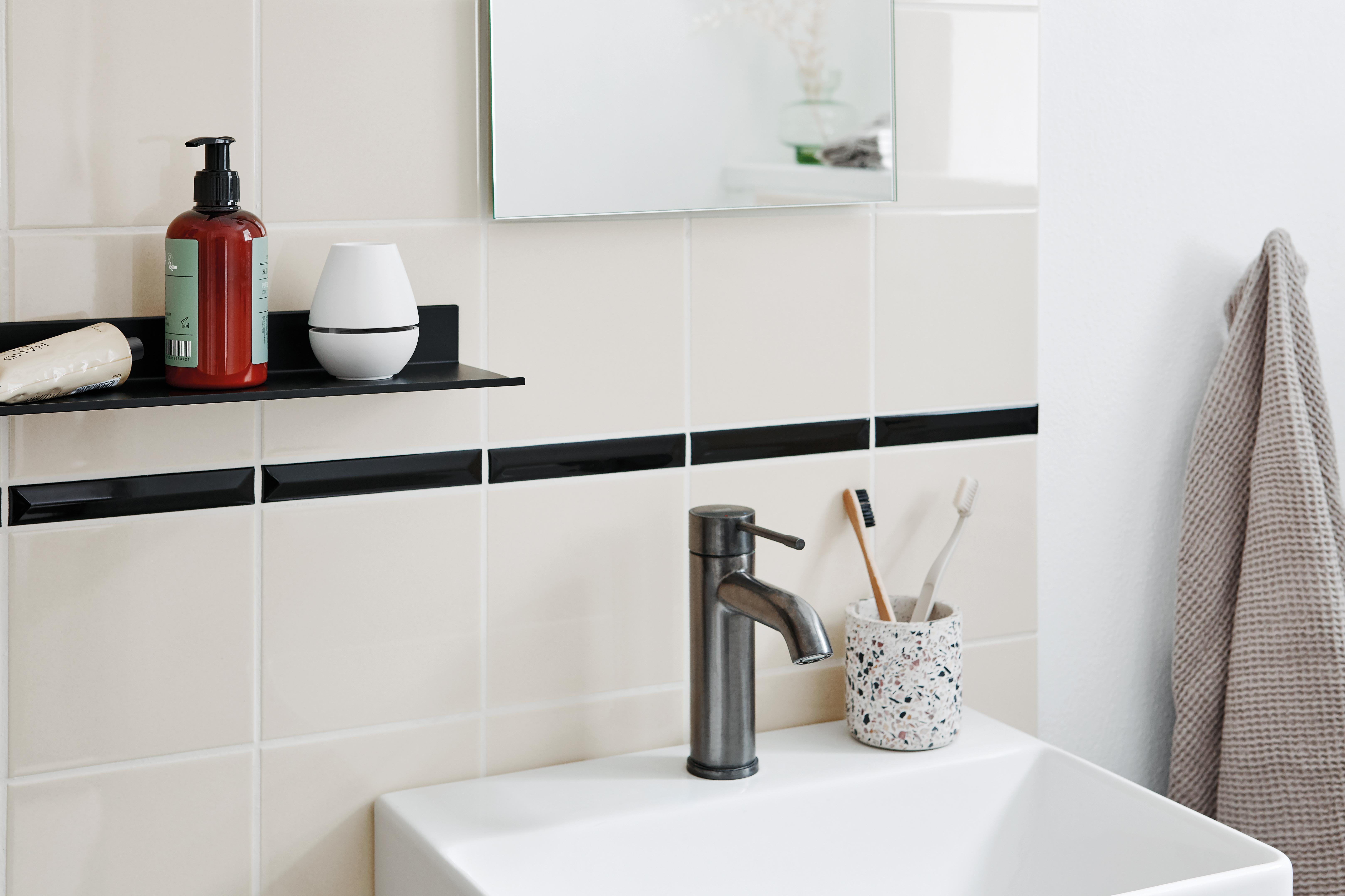 Badezimmer mit Waschbecken, Wasserhahn, Spiegel, Seife und Zahnbürstenhalter, alles an weißer Wand.