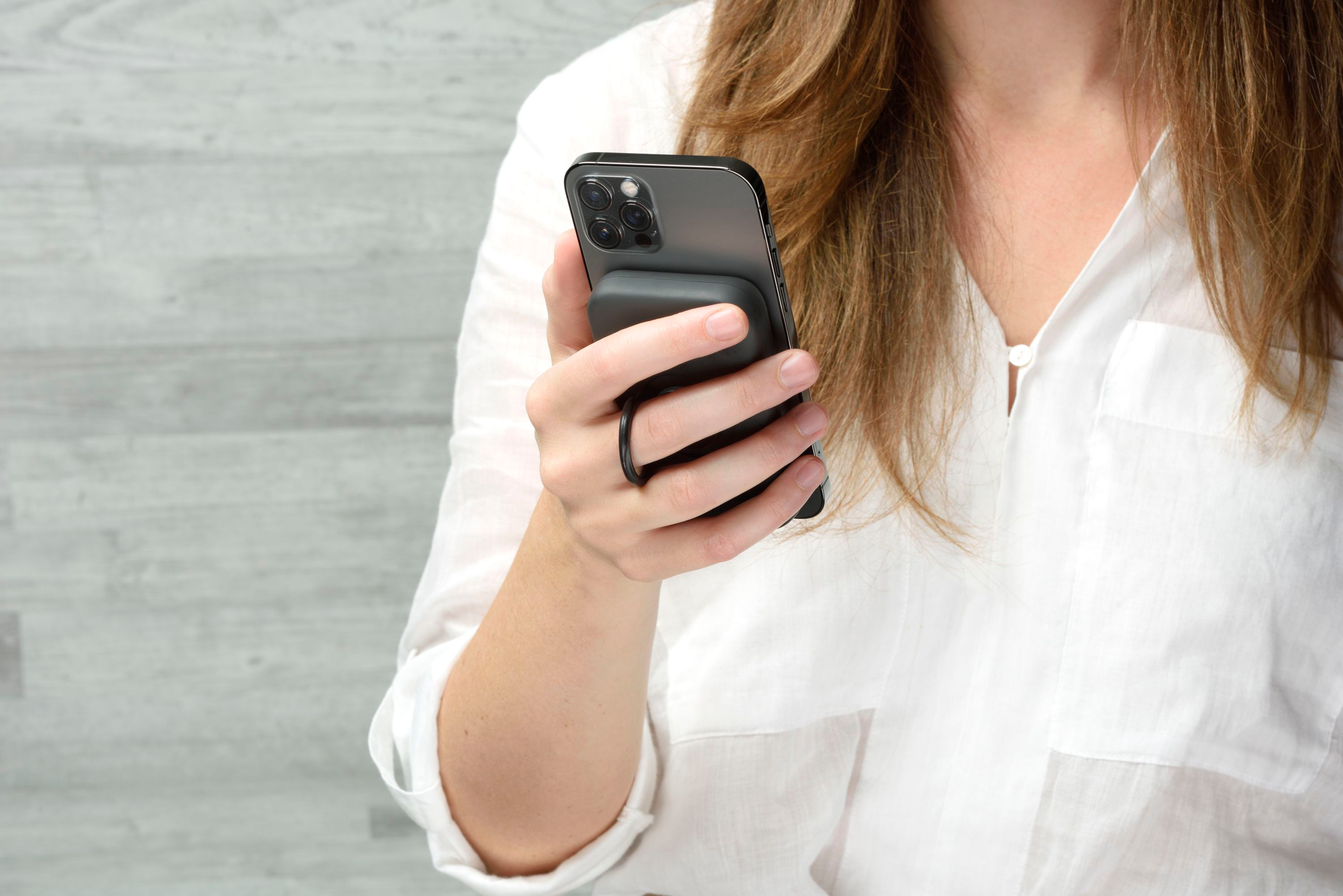 Eine Frau hält ein Smartphone mit einem angebrachten Ringgriff. Sie trägt ein weißes Hemd.