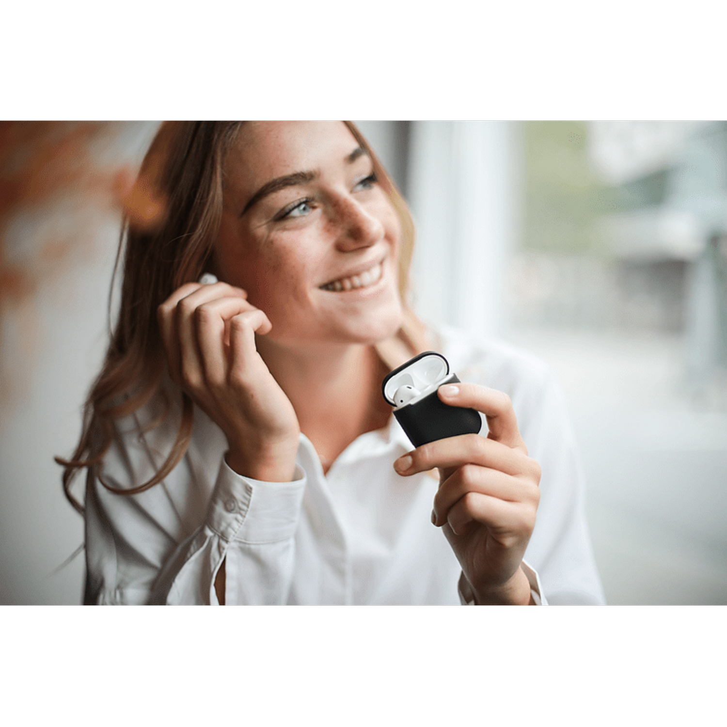 Mujer sonriendo, con auriculares, sosteniendo un estuche de carga negro.