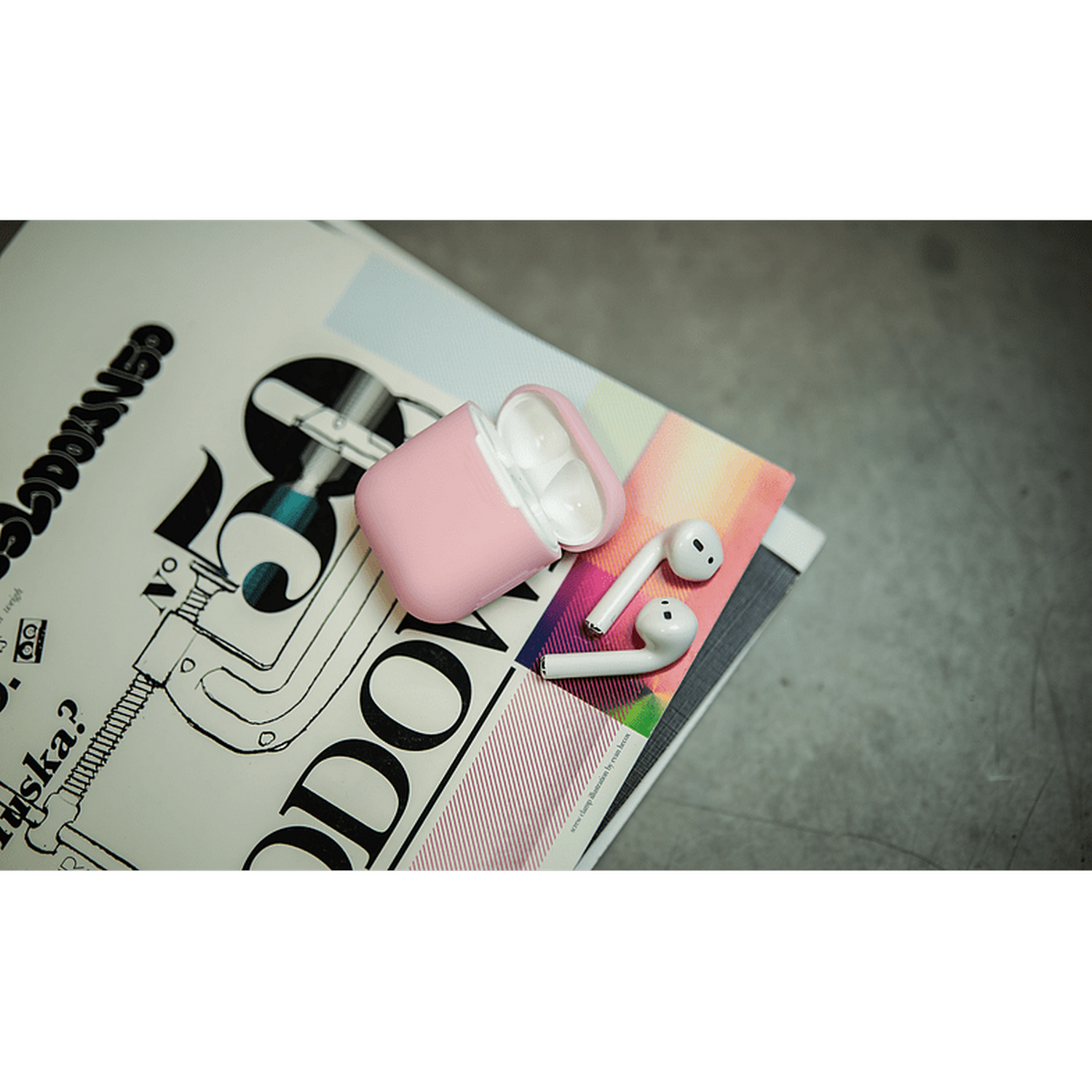 Estuche rosa de auriculares abierto en una revista con auriculares blancos al lado.