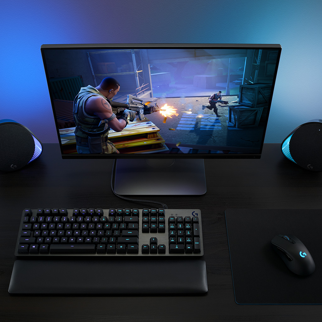 Configuration de jeu avec moniteur affichant une scène de jeu. Clavier, souris et enceintes visibles.