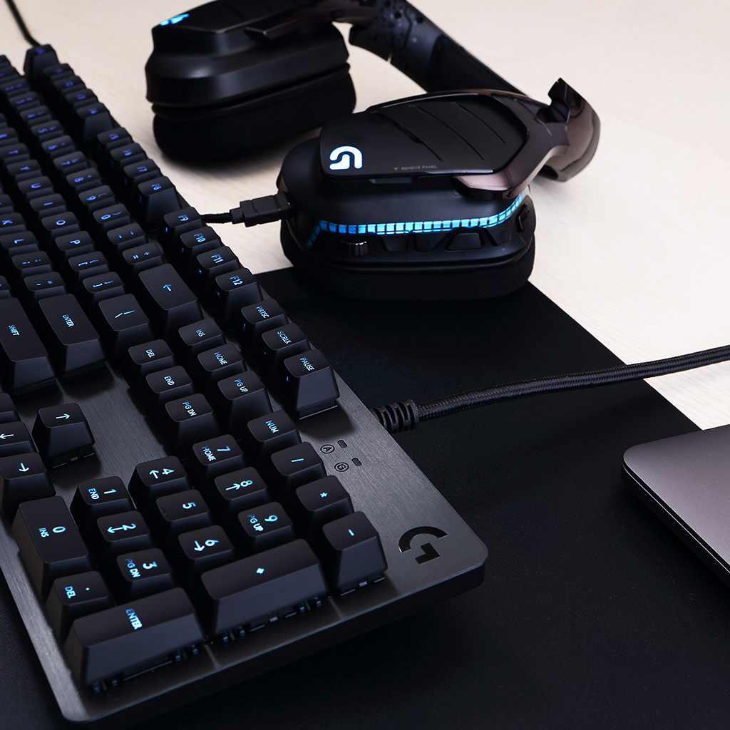 Gros plan sur un clavier et un casque de jeu sur une surface noire. Certaines touches sont éclairées.