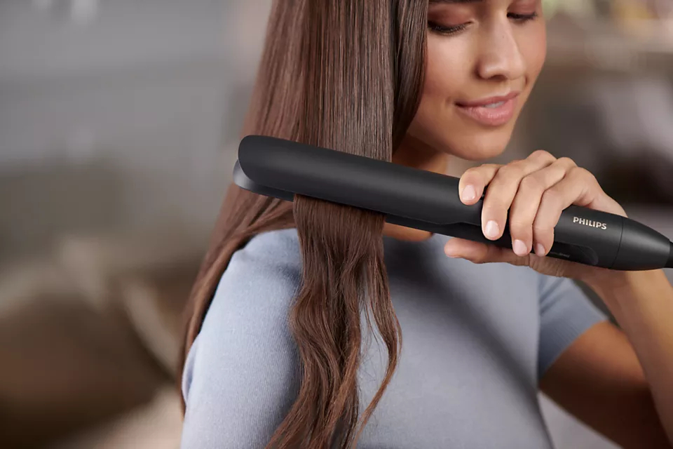 Frau benutzt schwarzen Philips Haarglätter auf braunem Haar.