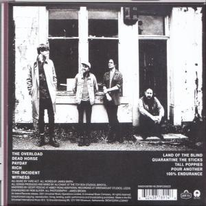 Rückseite einer CD. Zeigt eine Band von vier Männern vor einem Gebäude mit Songtiteln.