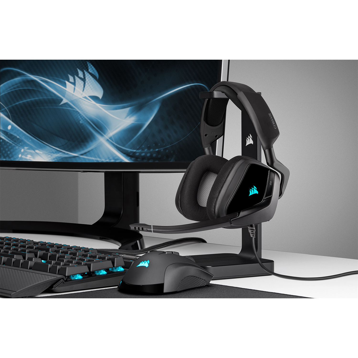 Configurazione gaming nera con cuffie su un supporto, mouse e tastiera. Monitor dietro.