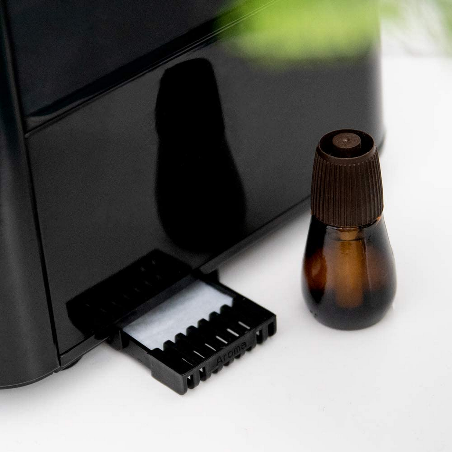 Un difusor de aroma negro con una pequeña botella de aceite esencial y una bandeja con almohadillas absorbentes blancas sobre una superficie blanca.