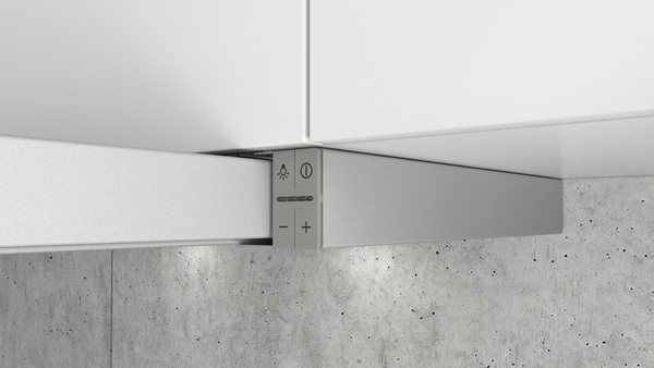 Close-up van een zilveren bedieningspaneel met knoppen op een witte kast met een betonnen muur.