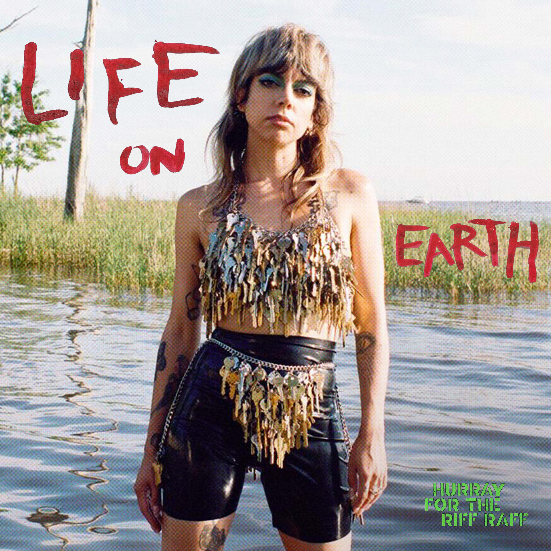 Nadrágban és kulcsos felsőben lévő nő, a vízben állva. "LIFE ON EARTH" felirat piros és zöld színben.