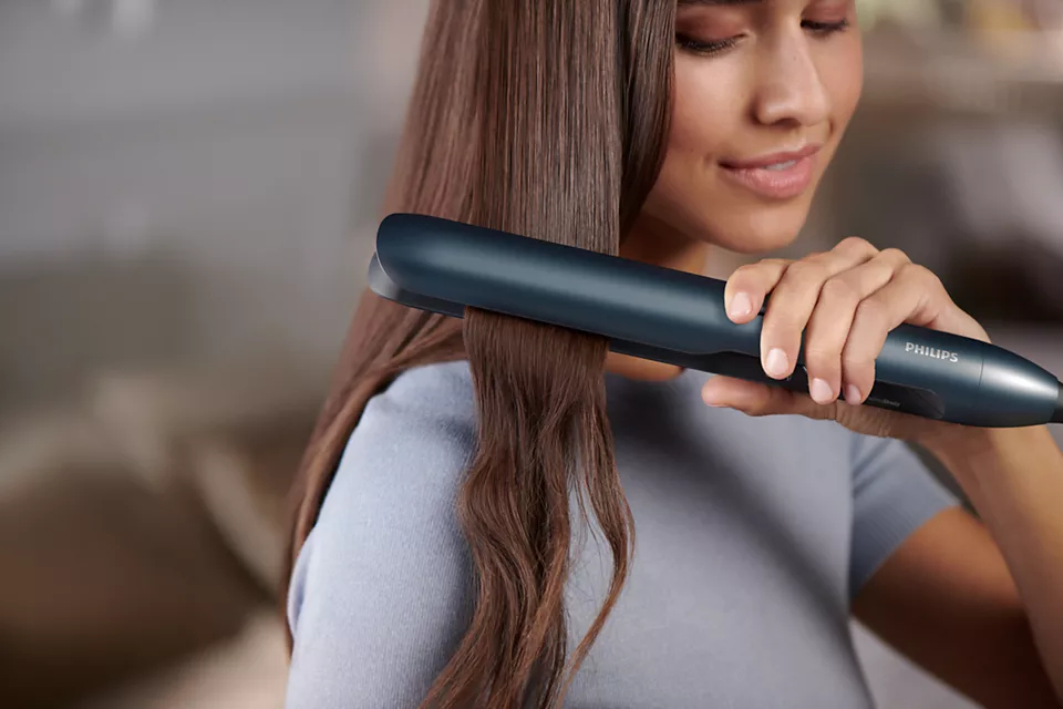 Frau benutzt einen Haarglätter, glättet ihr Haar.