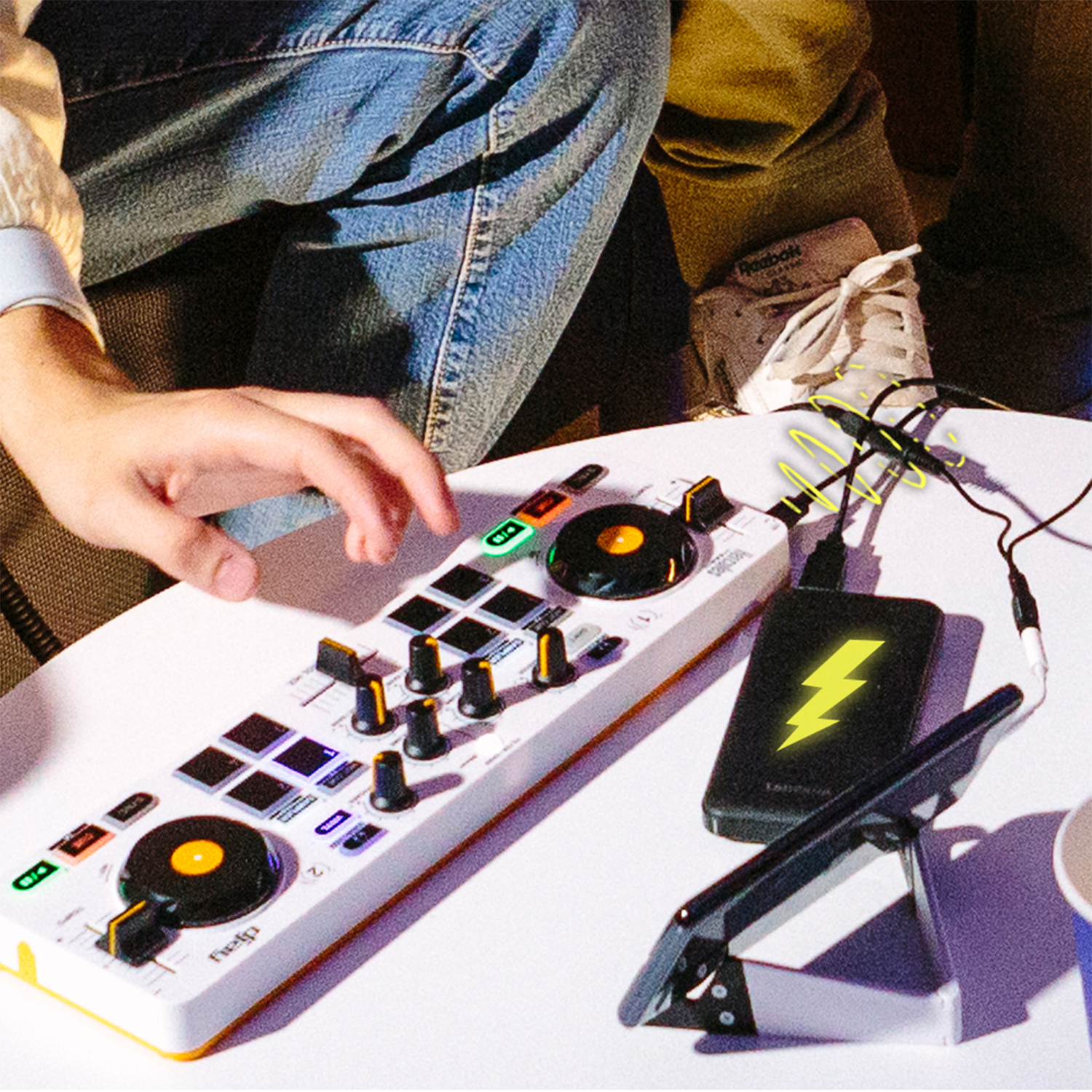 Persona che usa un controller DJ con tablet e power bank su un tavolo.